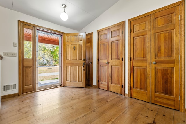 foyer featuring light wood finished floors, vaulted ceiling, and visible vents