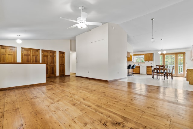 unfurnished living room with lofted ceiling, ceiling fan with notable chandelier, and light wood-type flooring