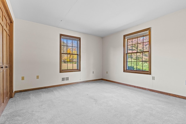 unfurnished room with baseboards, light carpet, visible vents, and plenty of natural light