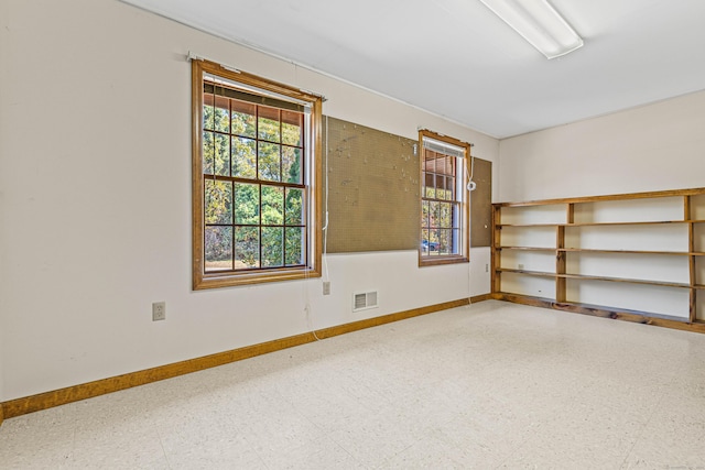 empty room featuring baseboards, tile patterned floors, visible vents, and a wealth of natural light