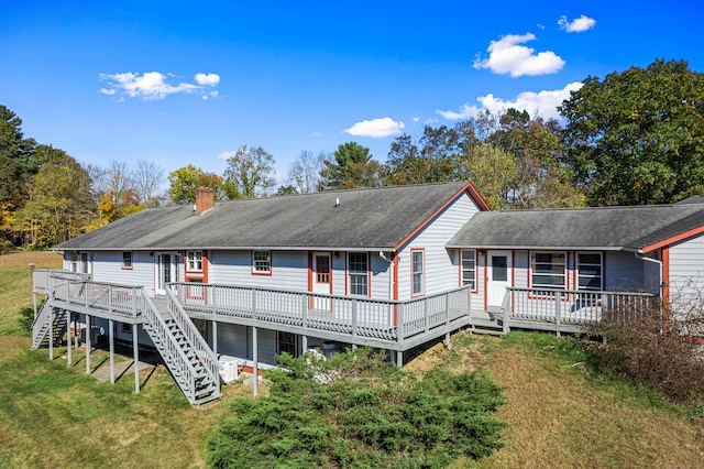 rear view of house featuring a chimney, a wooden deck, a lawn, a shingled roof, and stairs