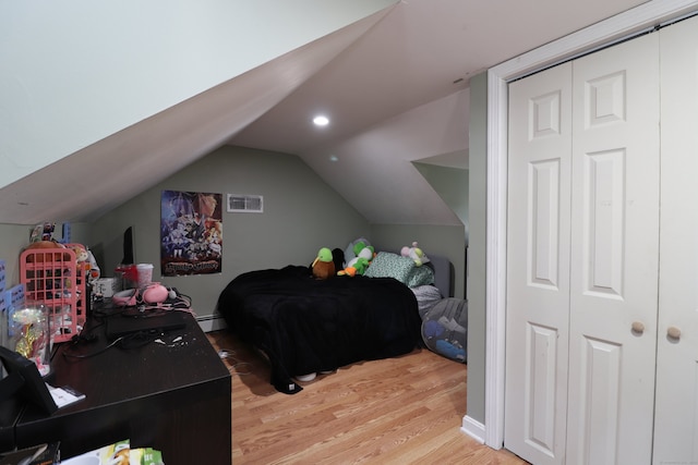 bedroom with wood-type flooring, a closet, vaulted ceiling, and a baseboard heating unit