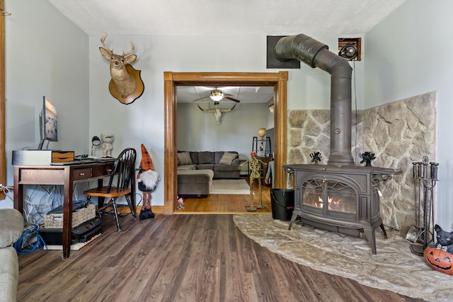 sitting room with ceiling fan, hardwood / wood-style flooring, a textured ceiling, and a wood stove