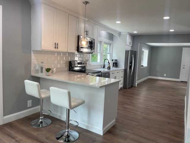 kitchen with dark hardwood / wood-style floors, kitchen peninsula, white cabinetry, appliances with stainless steel finishes, and a kitchen breakfast bar