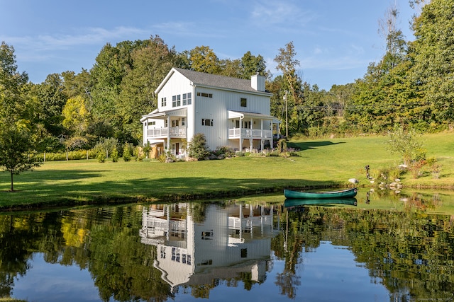 back of property with a water view, a balcony, and a lawn