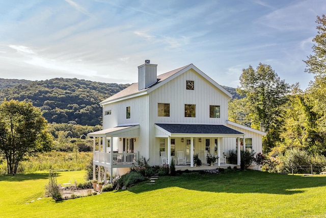 back of property featuring a mountain view, a yard, covered porch, a chimney, and board and batten siding