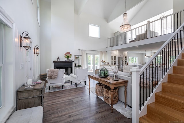 living area with stairs, a notable chandelier, a towering ceiling, and wood finished floors