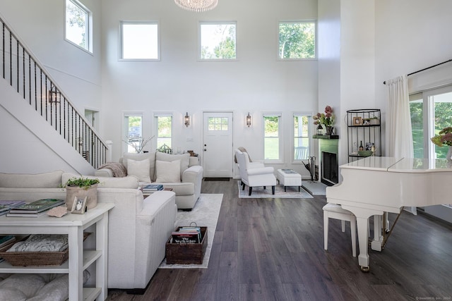 living area featuring dark wood-type flooring, a towering ceiling, a fireplace with raised hearth, and stairway