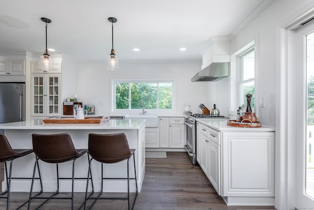 kitchen featuring a sink, wall chimney range hood, appliances with stainless steel finishes, white cabinetry, and a breakfast bar area