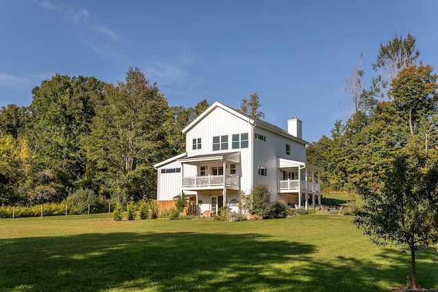 rear view of property featuring a yard, a balcony, board and batten siding, and a chimney