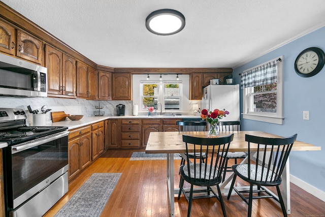 kitchen featuring tasteful backsplash, ornamental molding, appliances with stainless steel finishes, and light hardwood / wood-style flooring