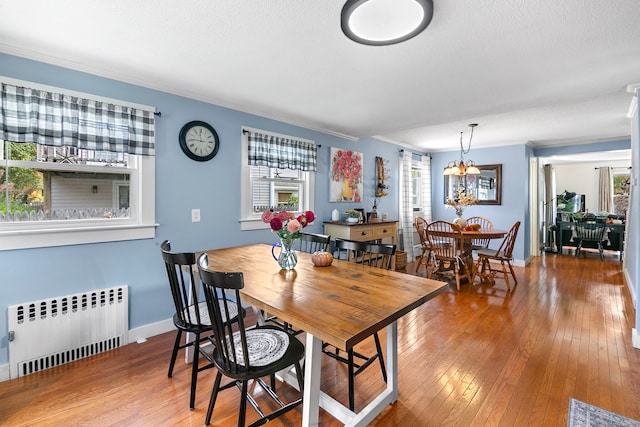 dining room featuring ornamental molding, radiator heating unit, wood-type flooring, a textured ceiling, and a notable chandelier