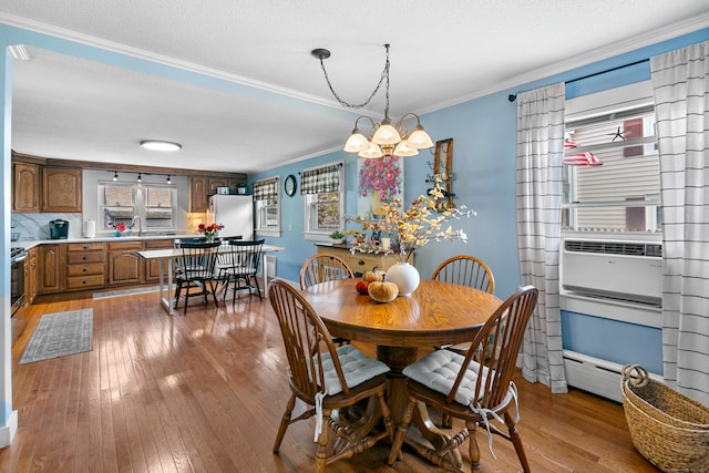 dining space with sink, a textured ceiling, light hardwood / wood-style flooring, a notable chandelier, and crown molding