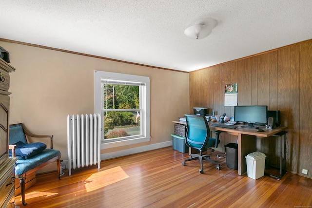 office with a textured ceiling, hardwood / wood-style floors, wooden walls, and radiator