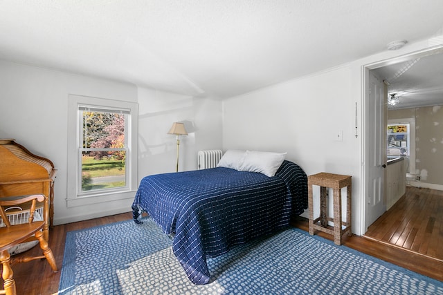 bedroom featuring dark wood-type flooring, radiator heating unit, and ensuite bathroom