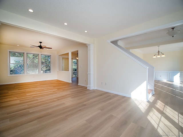 unfurnished living room featuring ceiling fan with notable chandelier, decorative columns, light hardwood / wood-style floors, and a textured ceiling