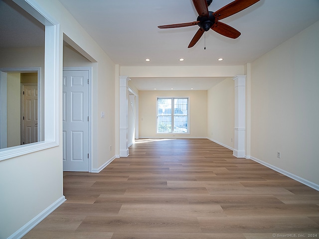 empty room with decorative columns, light wood-type flooring, and ceiling fan