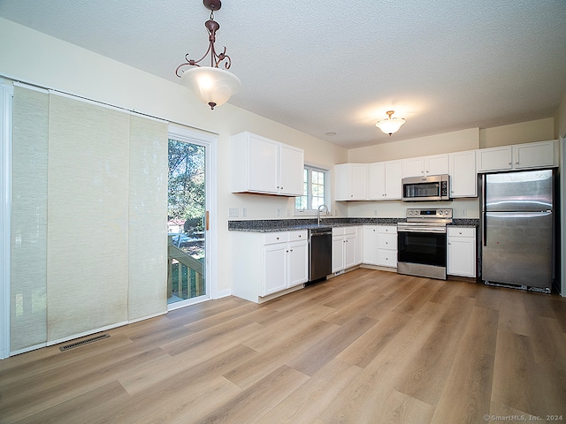 kitchen featuring decorative light fixtures, appliances with stainless steel finishes, light wood-type flooring, and white cabinetry