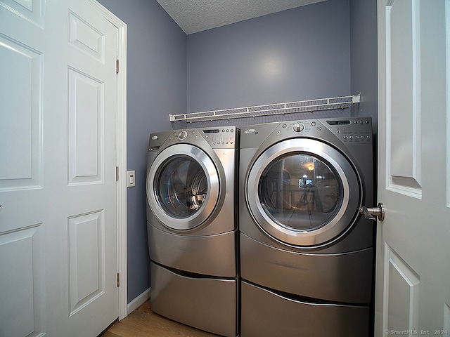 laundry room with washing machine and dryer, light wood-type flooring, and a textured ceiling