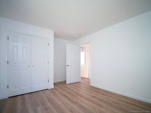 unfurnished bedroom featuring a closet, light hardwood / wood-style floors, and a textured ceiling