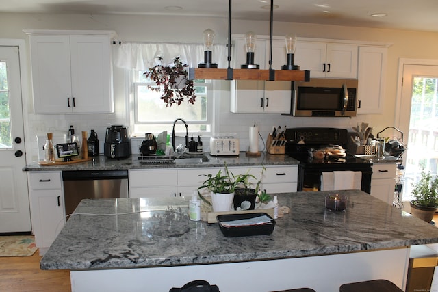 kitchen featuring light wood-type flooring, pendant lighting, dark stone countertops, stainless steel appliances, and white cabinetry