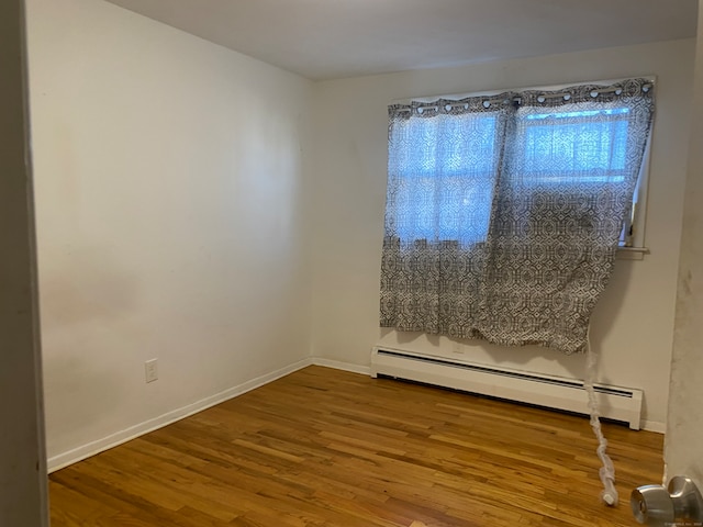 empty room featuring baseboard heating and hardwood / wood-style flooring