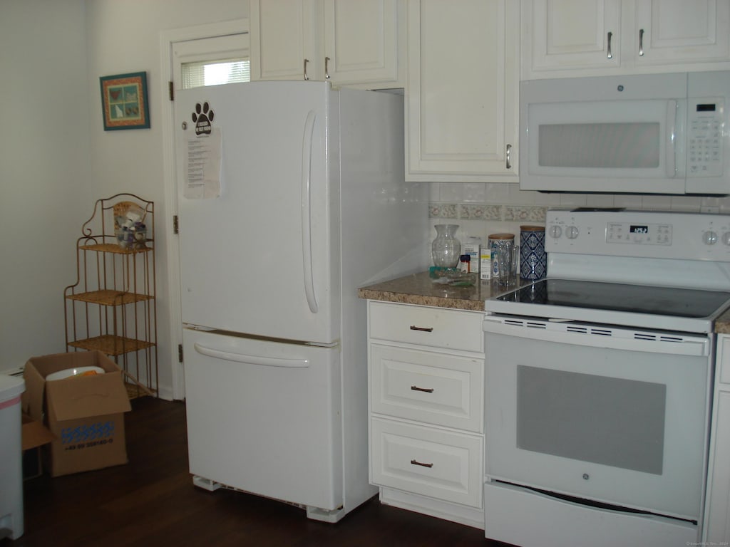 kitchen with white cabinets, dark hardwood / wood-style flooring, white appliances, and tasteful backsplash