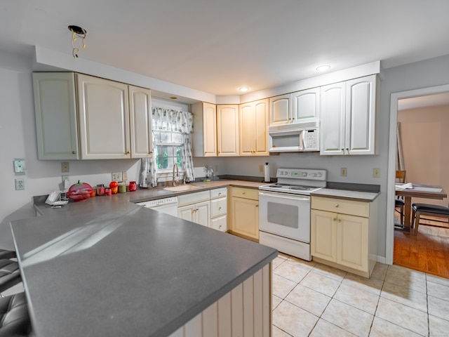 kitchen with sink, cream cabinetry, light tile patterned floors, and white appliances