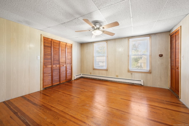 unfurnished bedroom with ceiling fan, a baseboard radiator, hardwood / wood-style floors, and wood walls