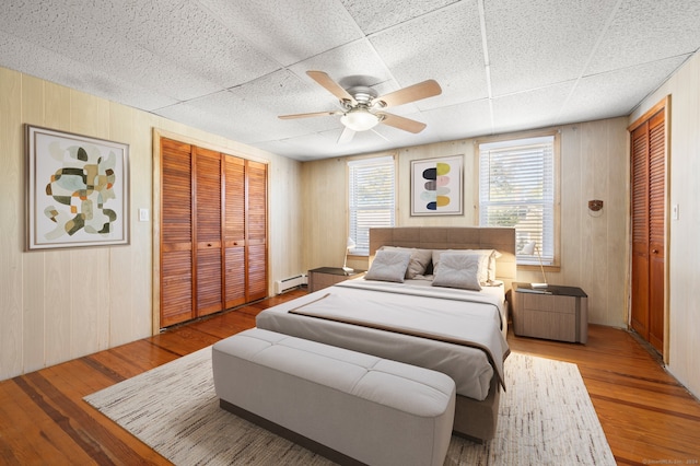 bedroom with ceiling fan, a baseboard radiator, wood walls, and light hardwood / wood-style floors