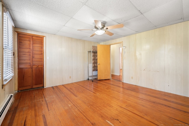 spare room with wood-type flooring, a baseboard radiator, a drop ceiling, and ceiling fan