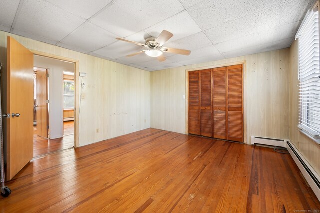 unfurnished bedroom with a drop ceiling, ceiling fan, hardwood / wood-style floors, a closet, and wooden walls