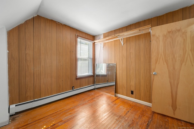 unfurnished room featuring lofted ceiling, hardwood / wood-style floors, a baseboard heating unit, and wooden walls