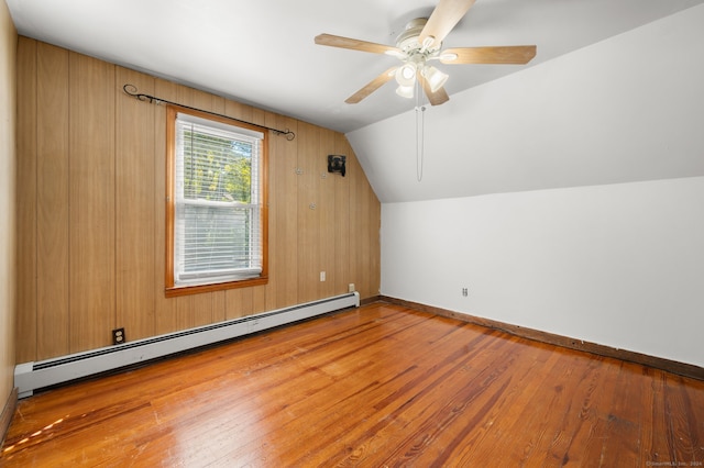 additional living space featuring wooden walls, ceiling fan, hardwood / wood-style floors, a baseboard heating unit, and vaulted ceiling