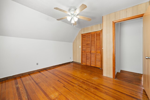 bonus room featuring wood-type flooring, wood walls, vaulted ceiling, and ceiling fan