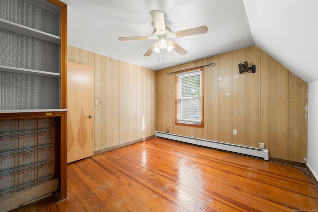 interior space with wood walls, light wood-type flooring, ceiling fan, vaulted ceiling, and a baseboard heating unit