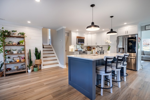 kitchen featuring appliances with stainless steel finishes, light wood-type flooring, decorative light fixtures, white cabinets, and a breakfast bar area