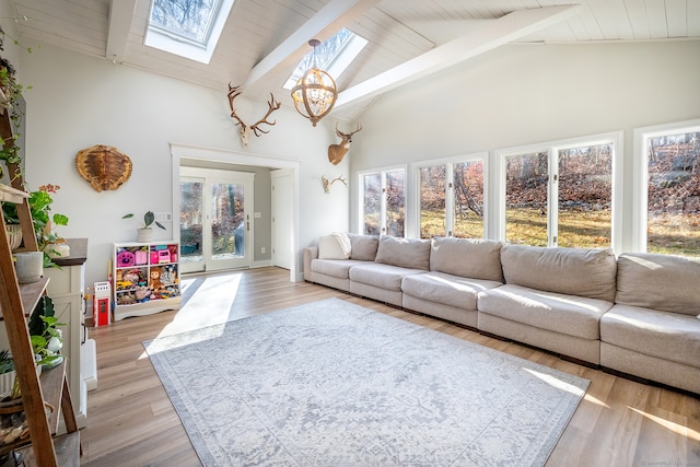 living room with high vaulted ceiling, a skylight, light hardwood / wood-style flooring, a notable chandelier, and beam ceiling