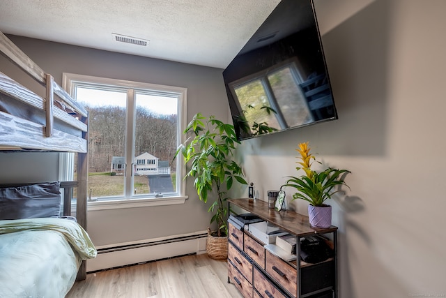 bedroom with light hardwood / wood-style flooring, a textured ceiling, and a baseboard heating unit