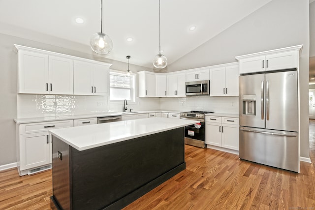 kitchen featuring appliances with stainless steel finishes, decorative light fixtures, light hardwood / wood-style flooring, white cabinetry, and a kitchen island