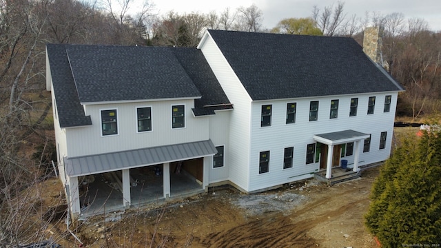 view of front of home with a shingled roof, a patio area, driveway, and a chimney