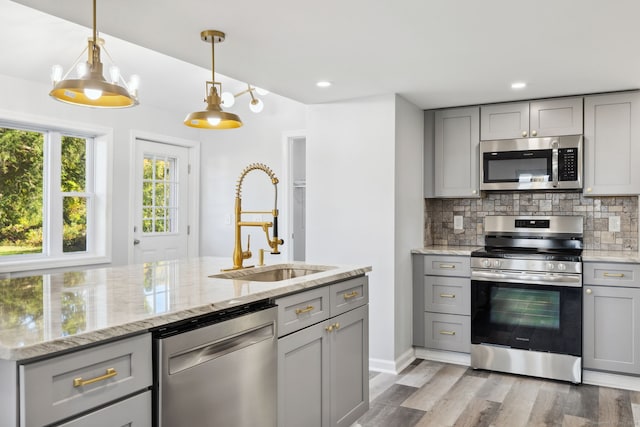 kitchen featuring light stone counters, tasteful backsplash, gray cabinetry, stainless steel appliances, and light hardwood / wood-style floors