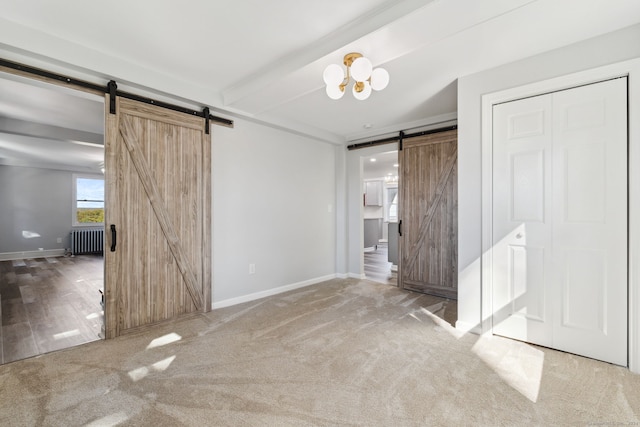 unfurnished bedroom featuring a barn door, carpet flooring, radiator heating unit, beam ceiling, and a closet