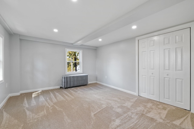 unfurnished bedroom with light carpet, beamed ceiling, a closet, and radiator heating unit