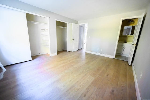 unfurnished bedroom with light hardwood / wood-style flooring, two closets, and ensuite bath