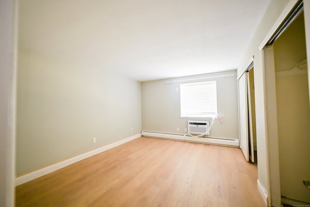 empty room with baseboard heating, a wall unit AC, and light hardwood / wood-style floors