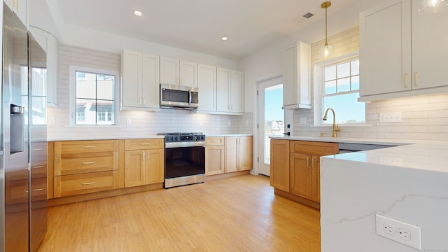 kitchen featuring light wood-type flooring, pendant lighting, backsplash, white cabinets, and appliances with stainless steel finishes