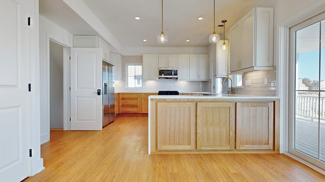 kitchen featuring light wood-type flooring, decorative backsplash, hanging light fixtures, appliances with stainless steel finishes, and light brown cabinetry