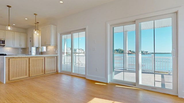 kitchen with a water view, light hardwood / wood-style floors, tasteful backsplash, light brown cabinets, and decorative light fixtures