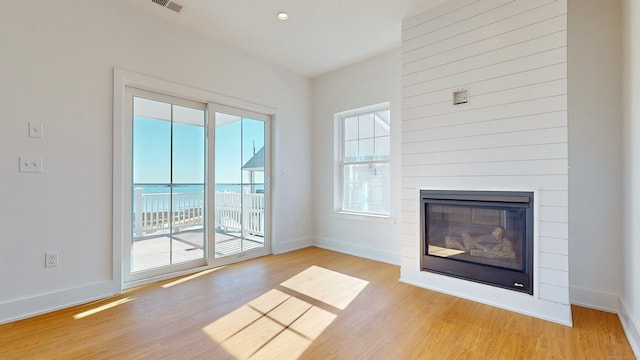 unfurnished living room with a fireplace, light hardwood / wood-style floors, and a water view